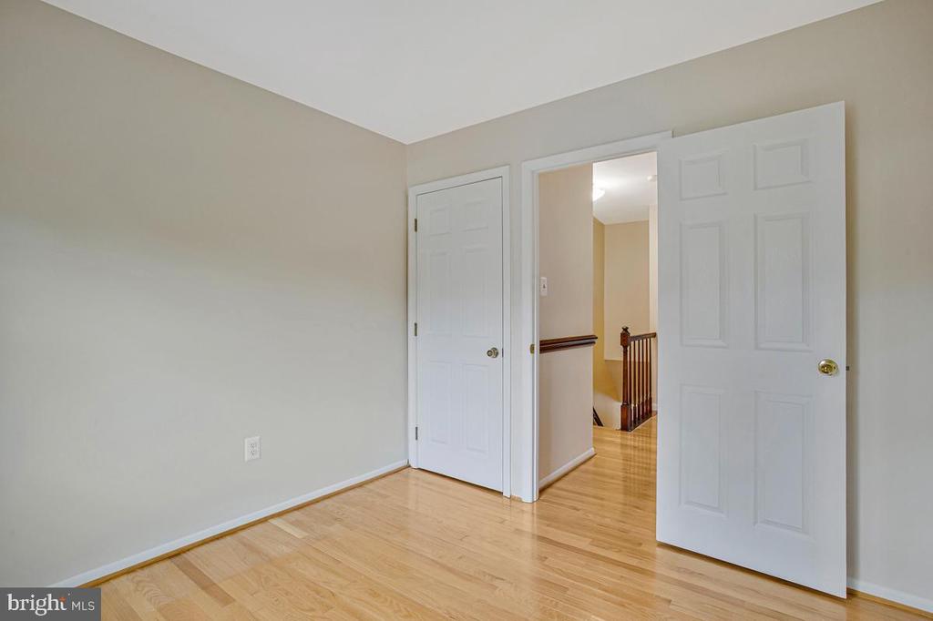 Empty room with light hardwood floors and an open doorway to a hall with a wooden railing.