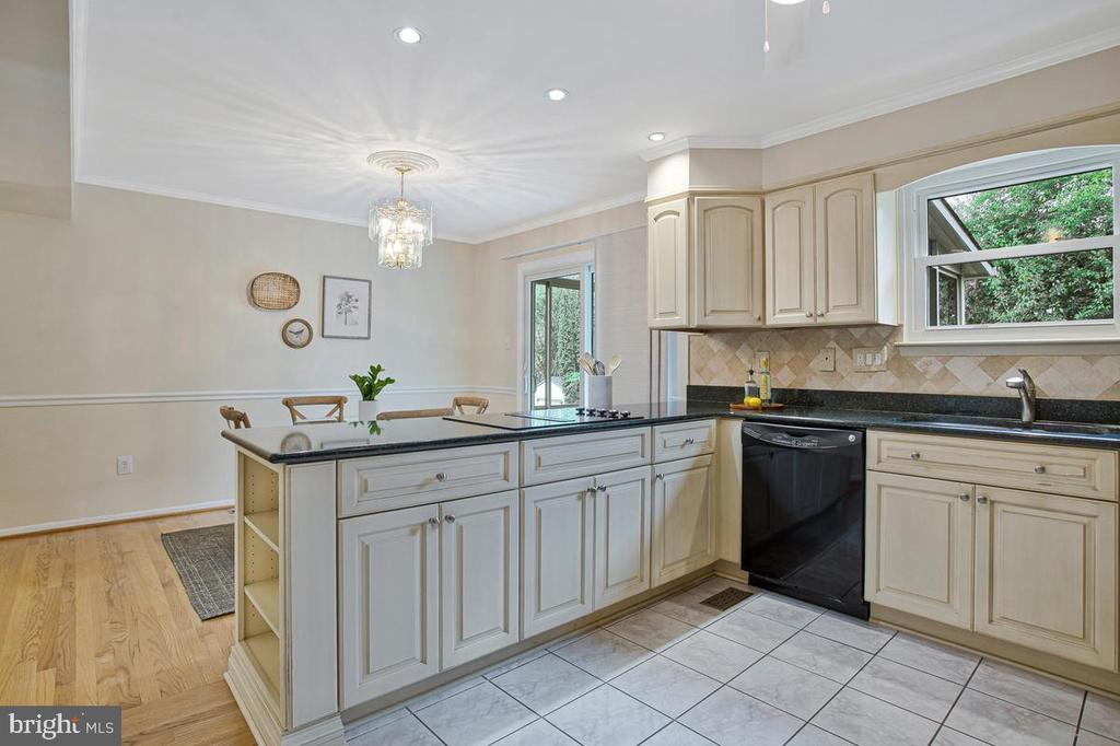 Kitchen with a granite-topped island, gas cooktop, cream cabinets, and windows overlooking greenery.