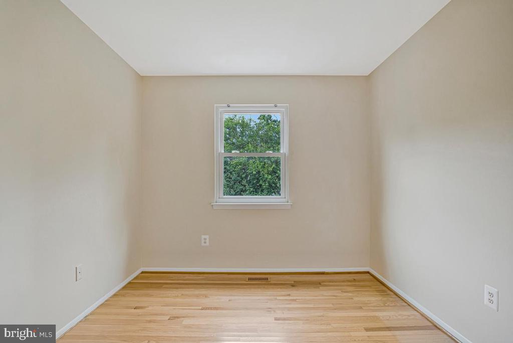 Empty room with light hardwood floors and a window overlooking leafy trees.