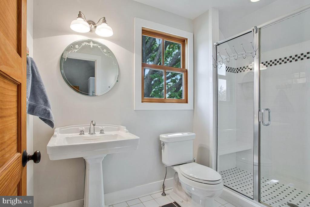 Bathroom with a glass-enclosed shower, pedestal sink, and wood-trimmed window.