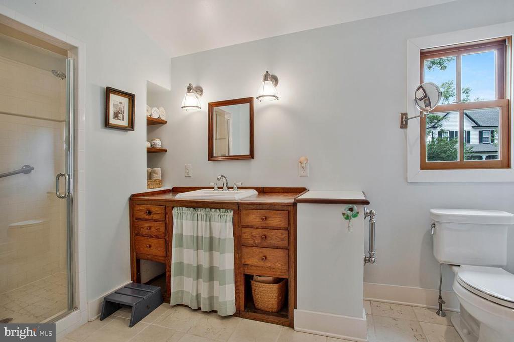 Bathroom with a wood vanity, striped sink skirt, glass shower, and wood-framed window.