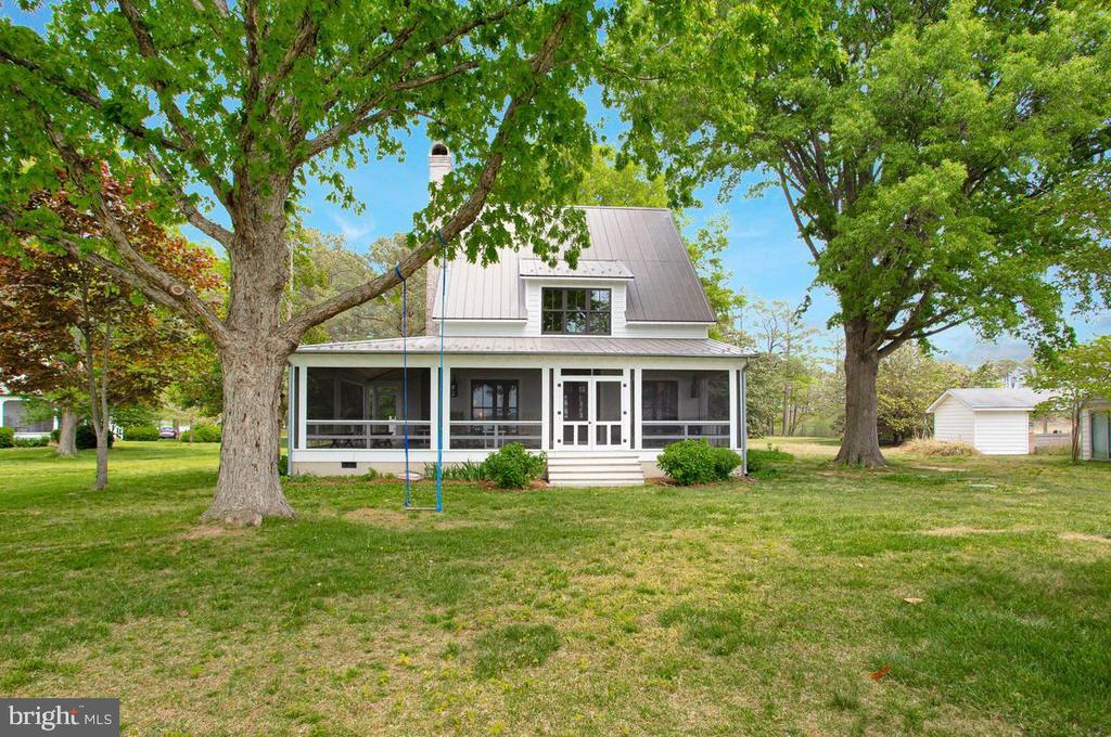 House with a screened-in porch beneath mature trees, with a broad lawn and detached outbuilding.