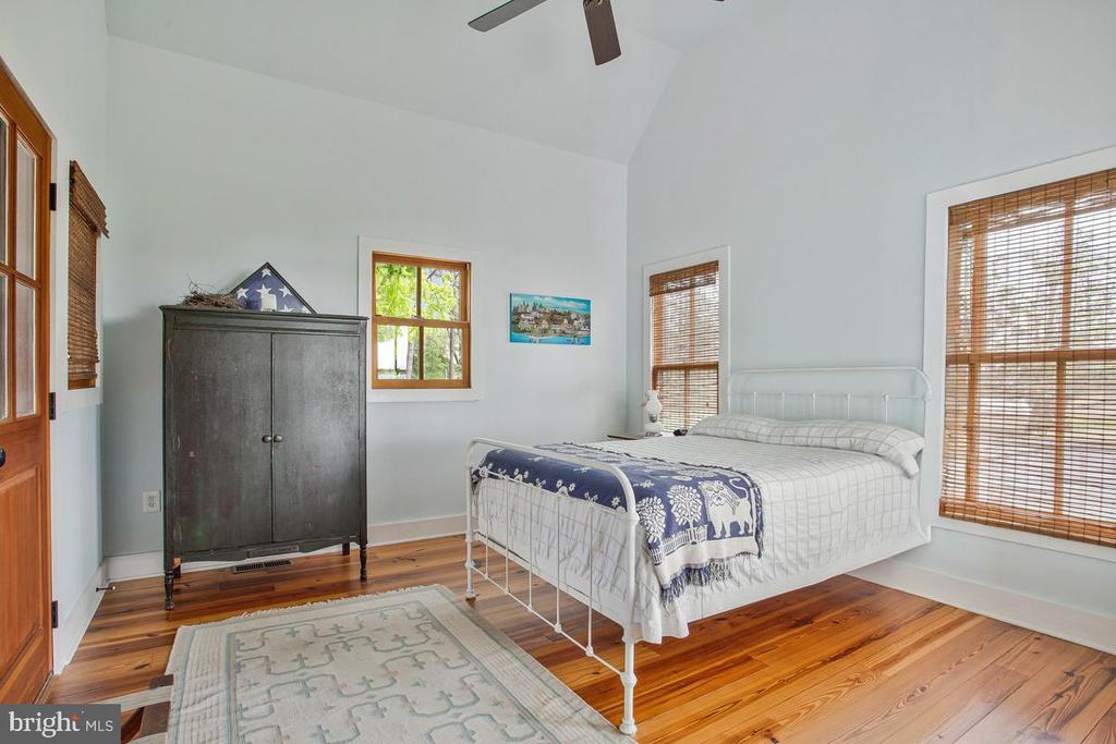 Bedroom with a white metal bed, patterned bedding, dark wardrobe, and warm wood floors.