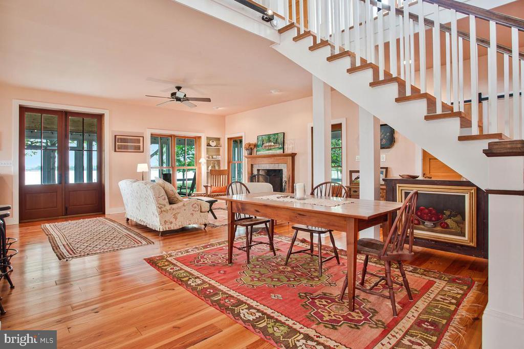 Open living and dining room with a fireplace, hardwood floors, patterned rugs, and a prominent staircase.