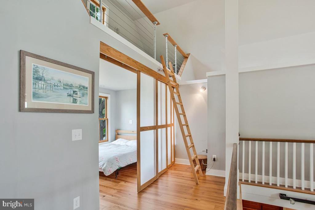 Bedroom and loft landing with a wood ladder, white partition, and warm wood floors.