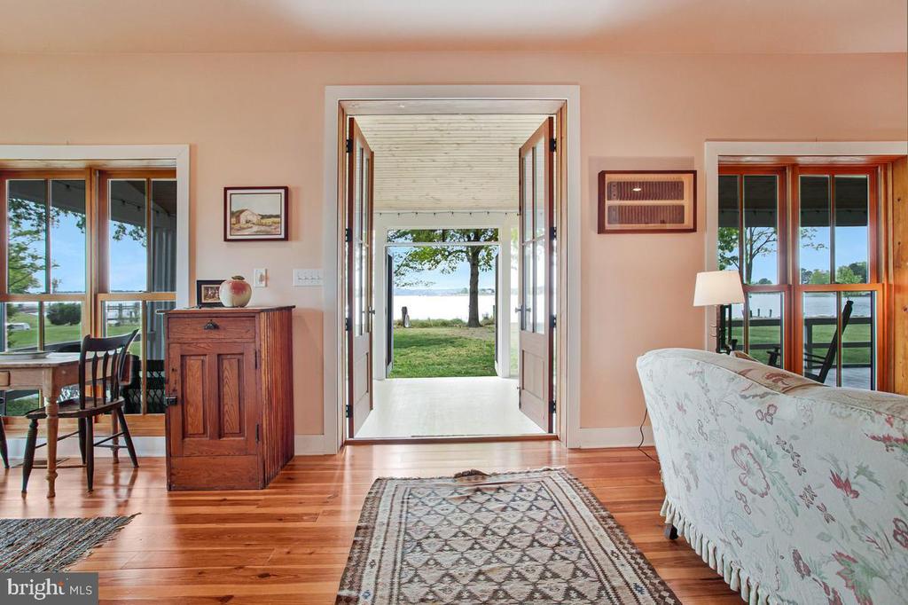 Living room with hardwood floors and open doors framing a grassy waterfront view.