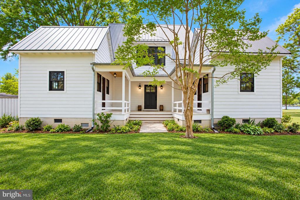 White house with metal roof, recessed porch, black front door, and a tree in the front lawn.