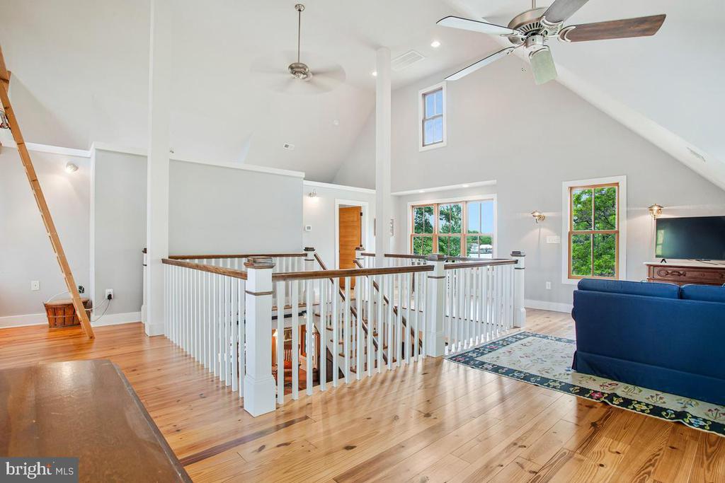 Upper-level loft with vaulted ceilings, hardwood floors, white stairwell railing, and a blue sofa by the windows.