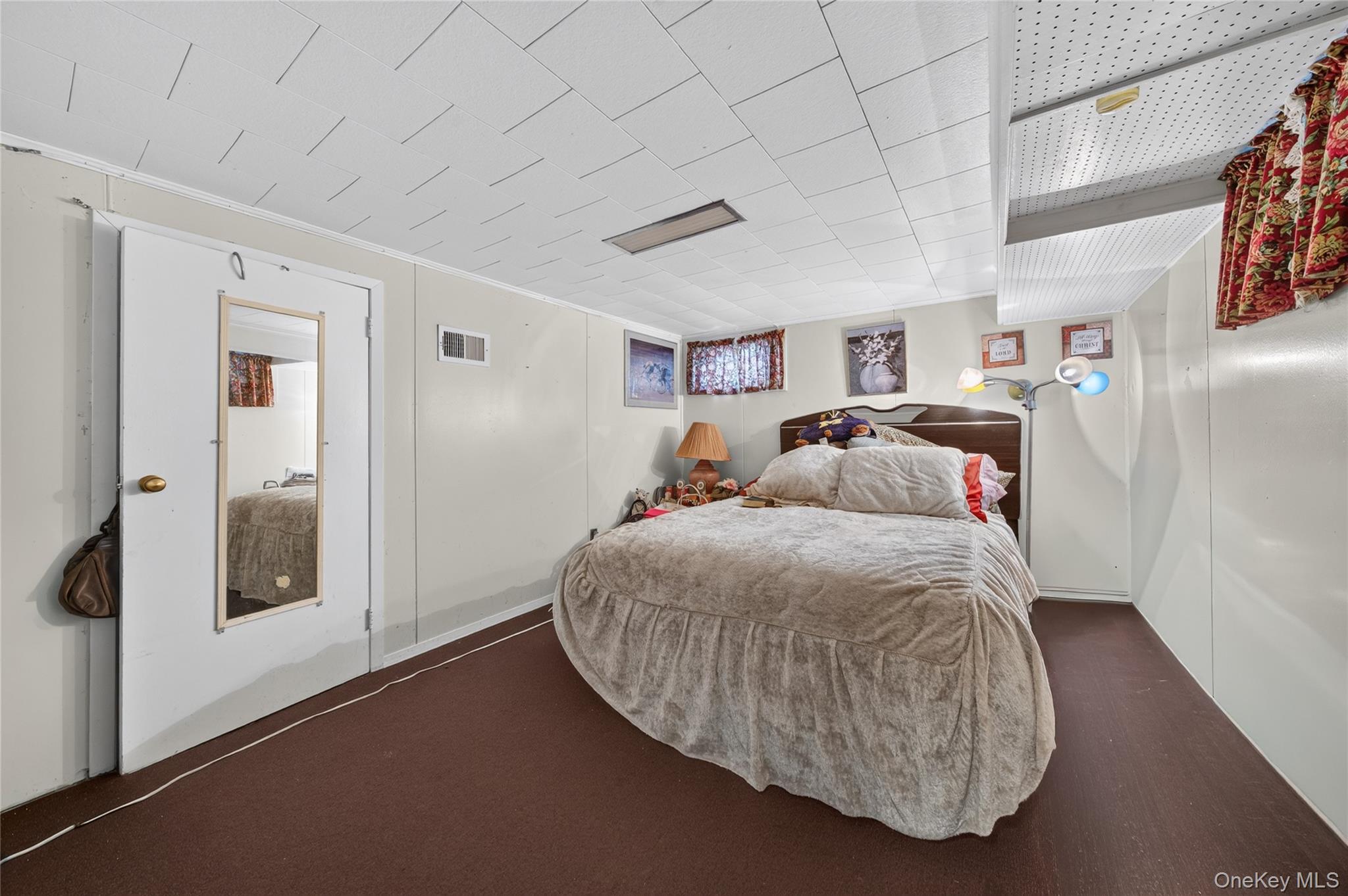 Bedroom with a large quilt-covered bed, mirrored door, and patterned curtains.