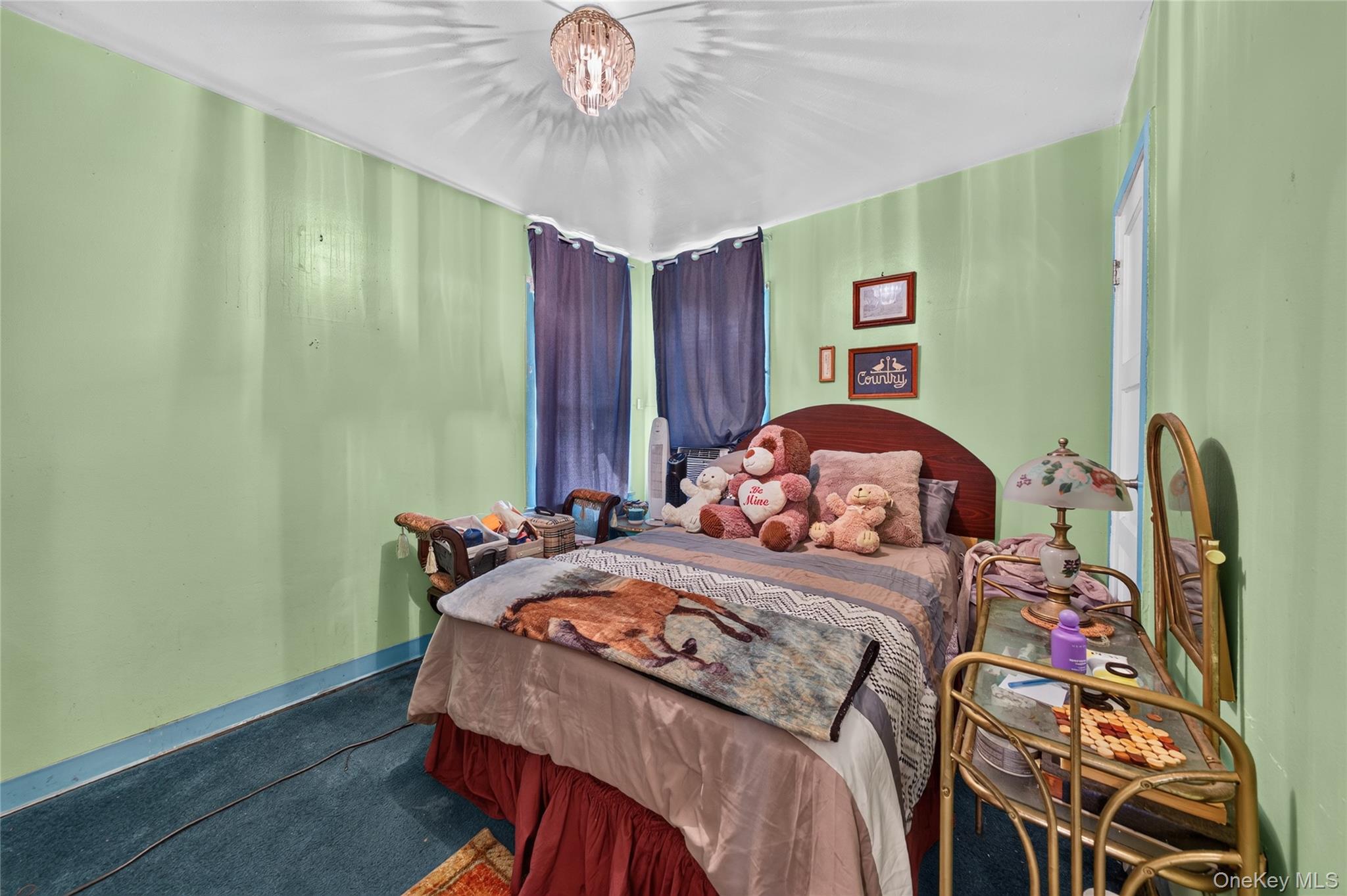 Bedroom with pale green walls, blue curtains, and a bed piled with stuffed animals.