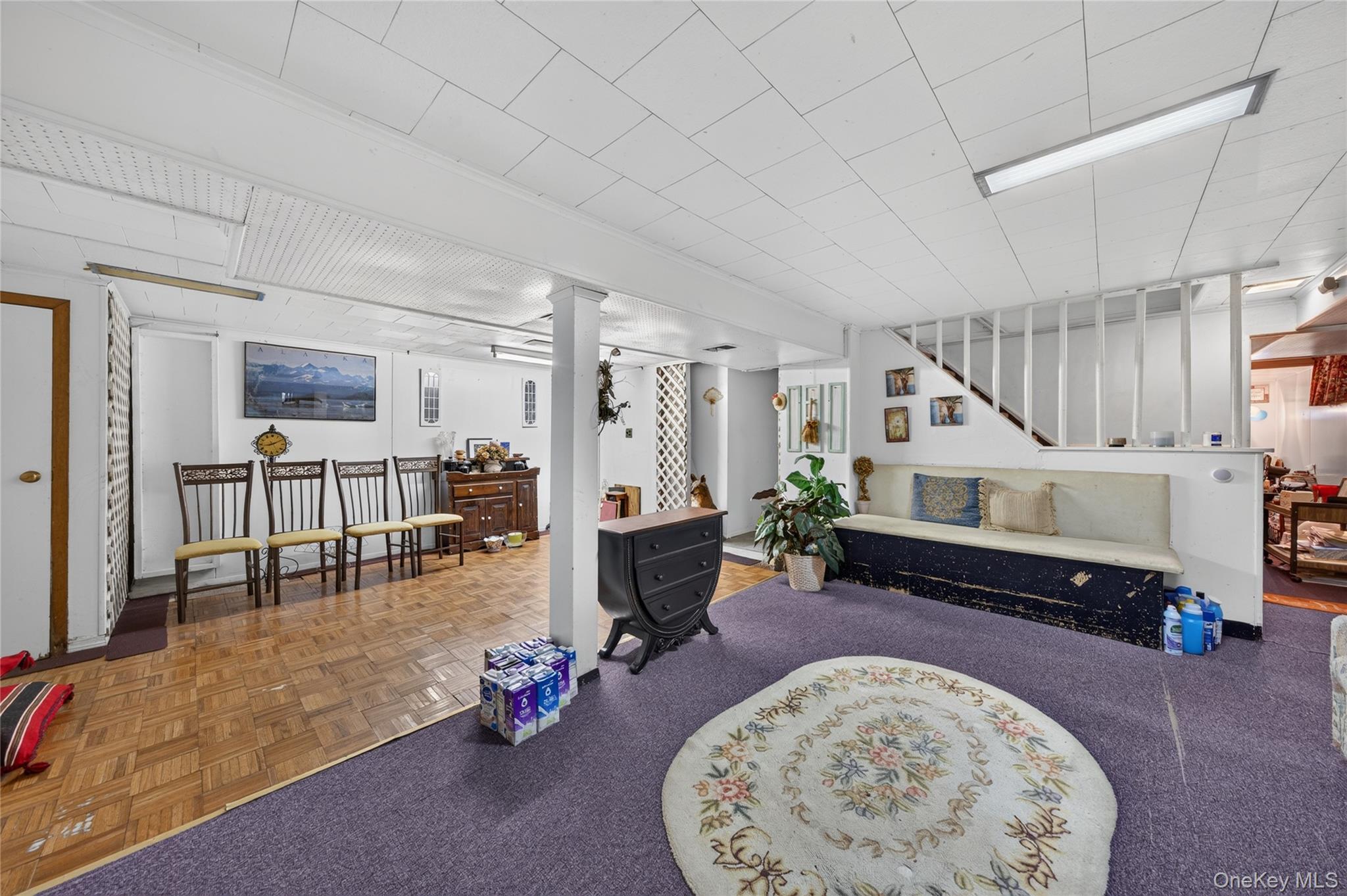 Furnished basement recreation room with purple carpet, floral rug, built-in bench, and adjoining dining area.