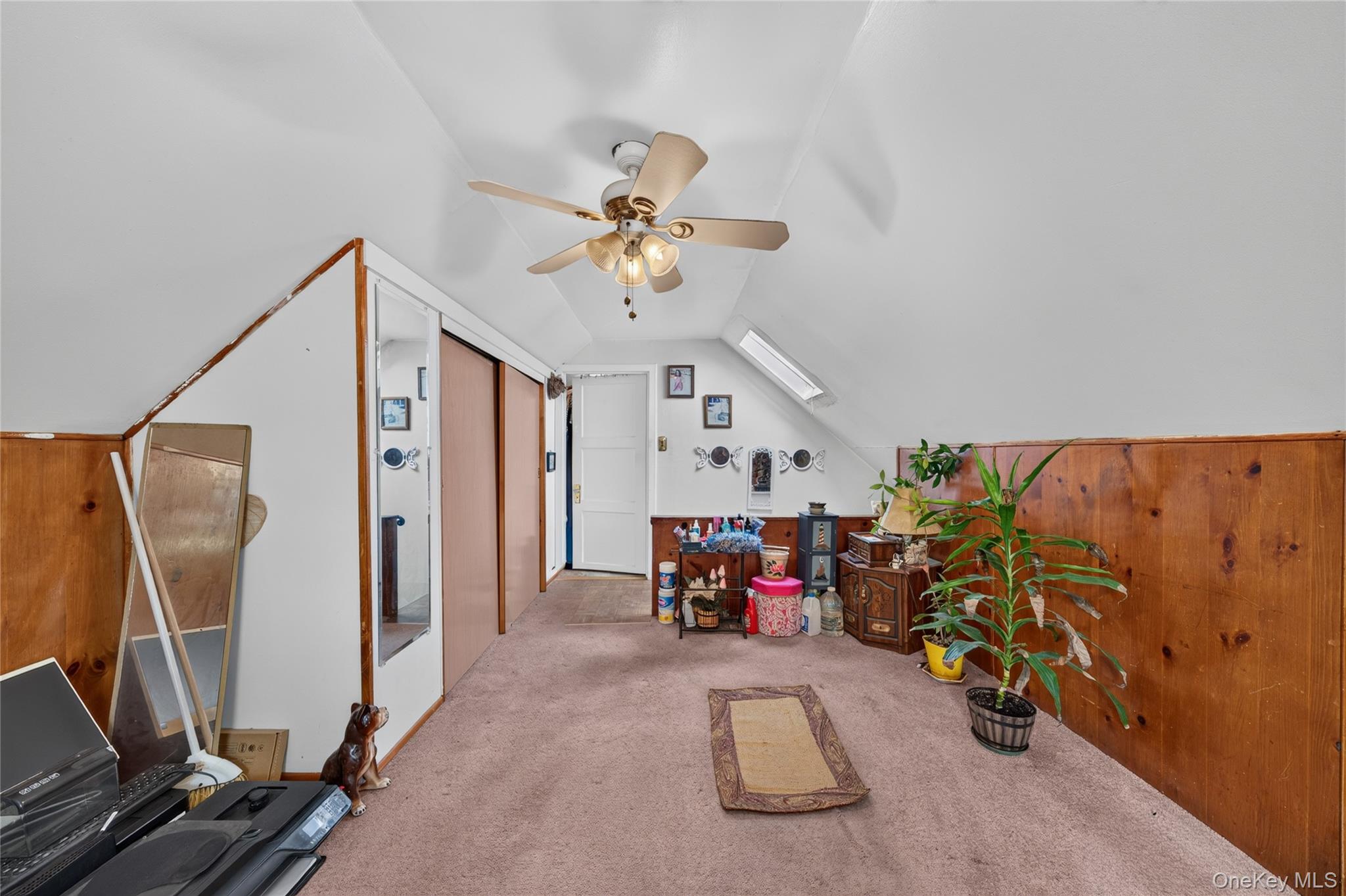 Finished attic room with sloped ceilings, wood paneling, carpet, and a ceiling fan.