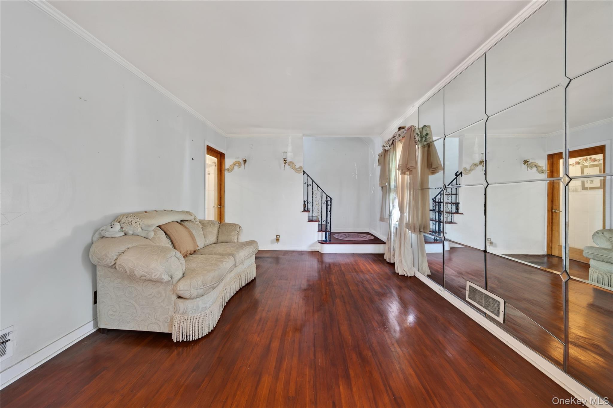 Living room with mirrored wall, cream sofa, hardwood floors, and staircase.