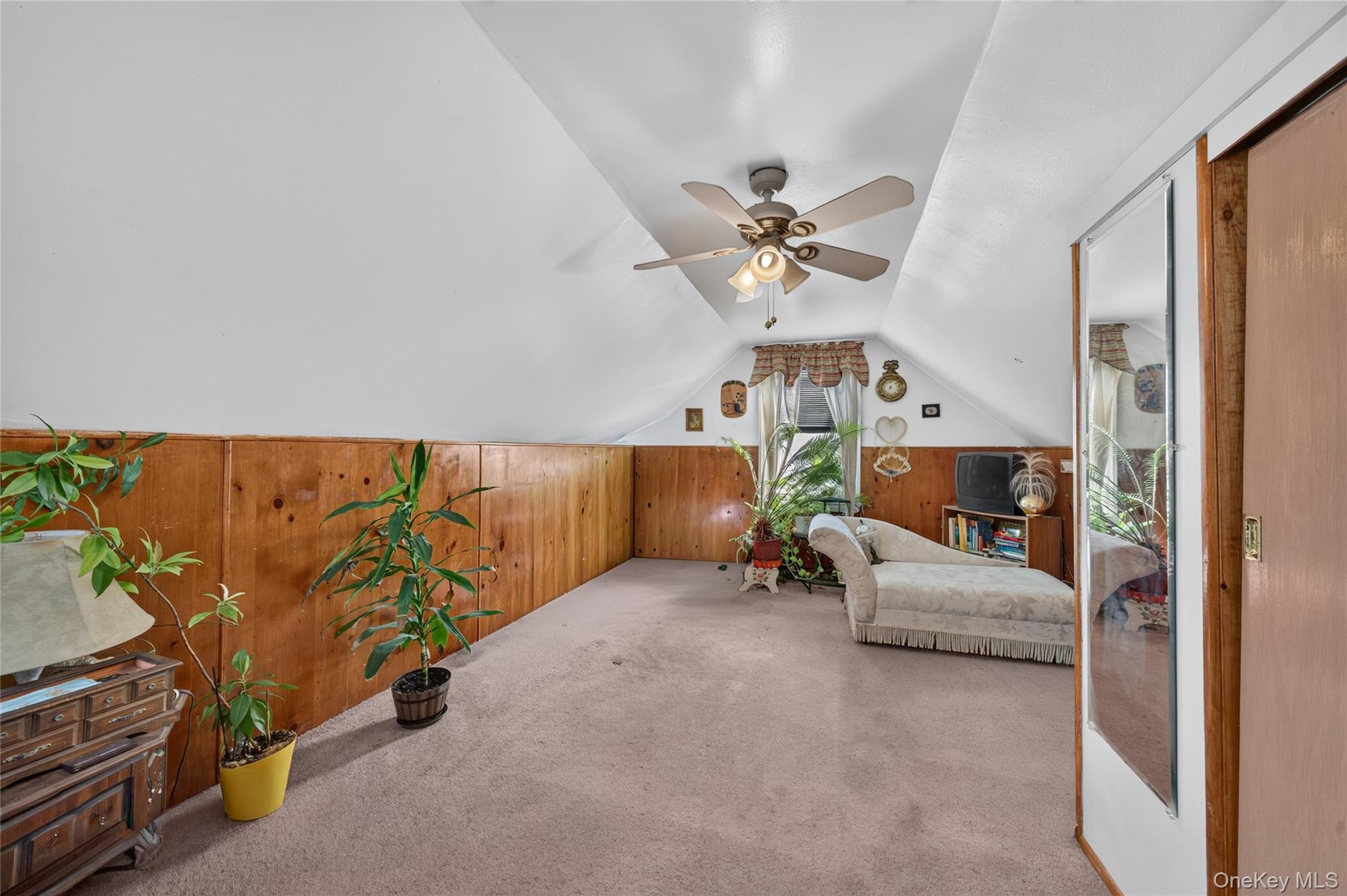 Furnished attic sitting room with sloped ceilings, wood paneling, a chaise lounge, and potted plants.
