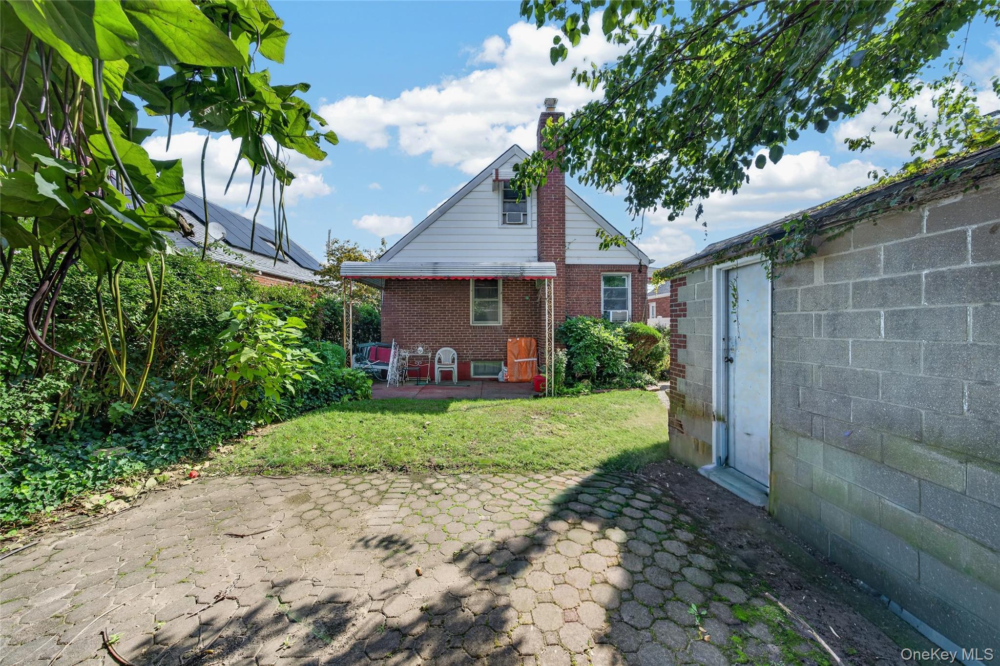 Brick house backyard with a covered patio, paved courtyard, lawn, and detached outbuilding.