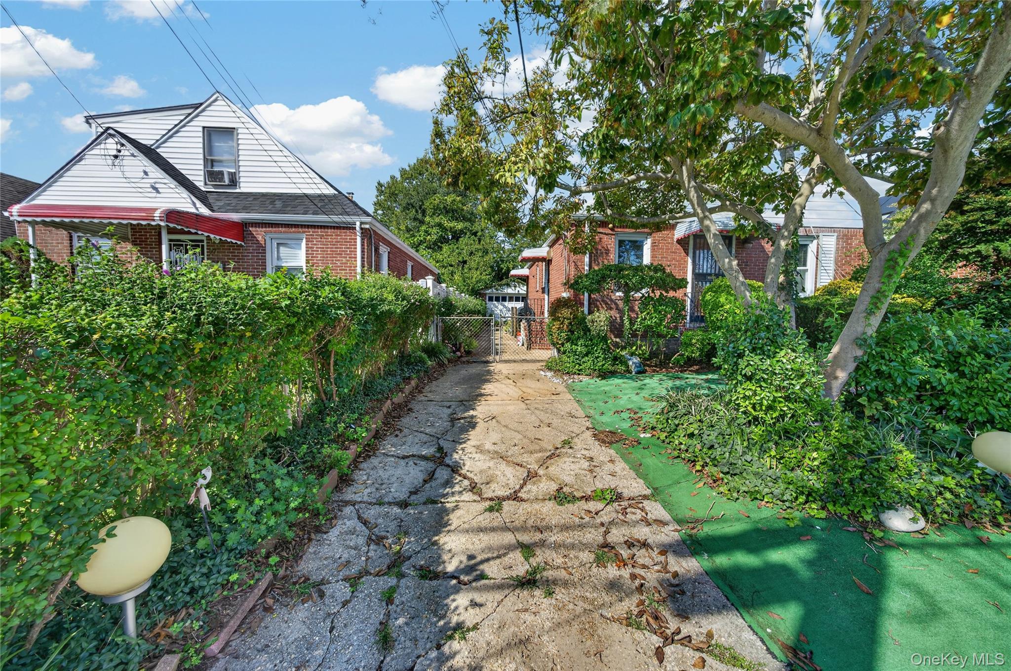 Brick home beyond a cracked stone walkway, framed by dense hedges and a large shade tree.