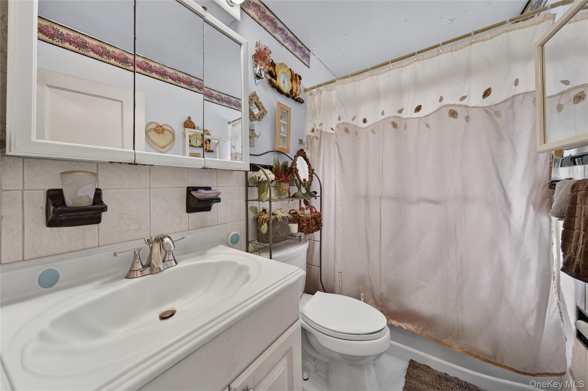 Bathroom with a white vanity and toilet beside a curtained bathtub.