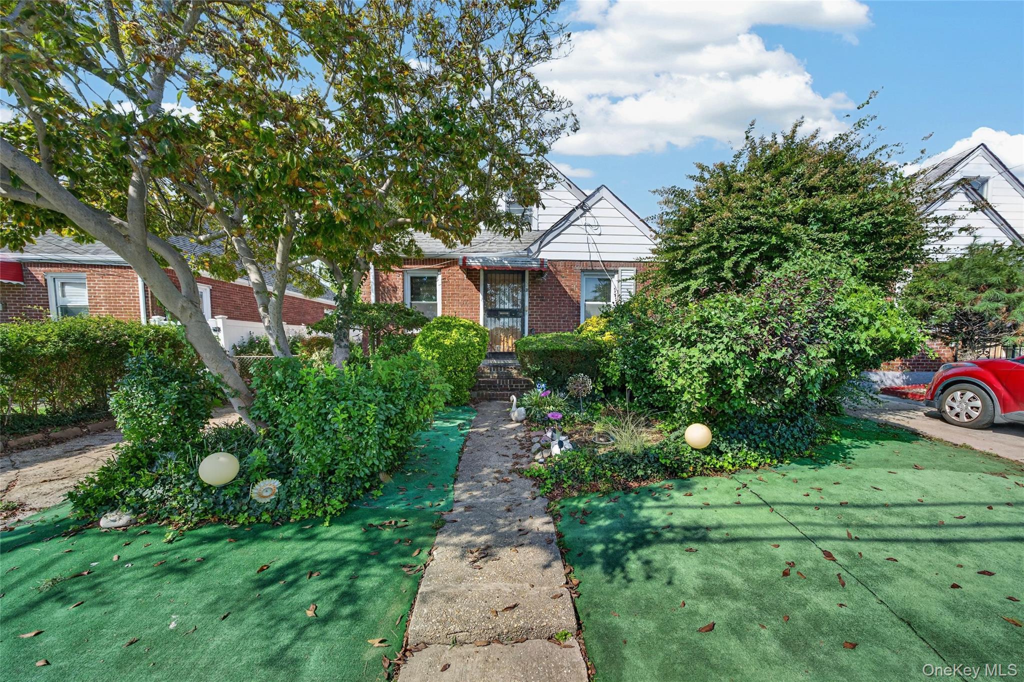 Brick house with white gables, dense landscaping, and a concrete walkway to the front entrance.