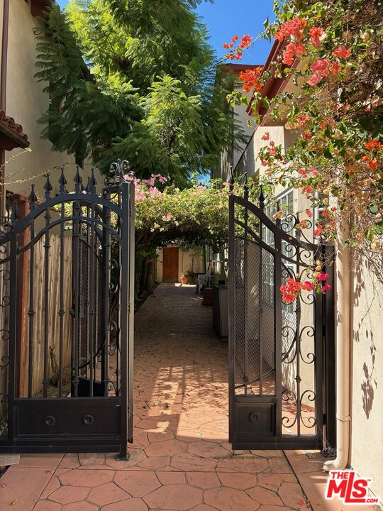 Guesthouse entrance beyond an open wrought-iron gate, framed by flowering vines and greenery.