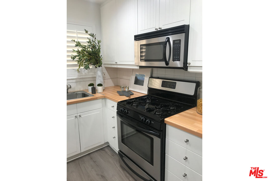 Kitchen with white cabinets, butcher-block counters, and a black gas range beneath a stainless-steel microwave.