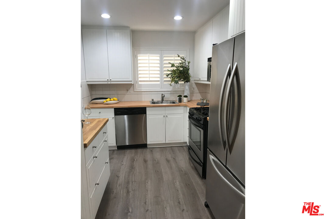 Kitchen with white cabinets, gray flooring, stainless-steel appliances, and a sink beneath shuttered windows.