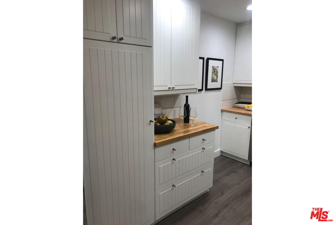 Kitchen with white paneled cabinets, warm wood countertops, and dark wood flooring.