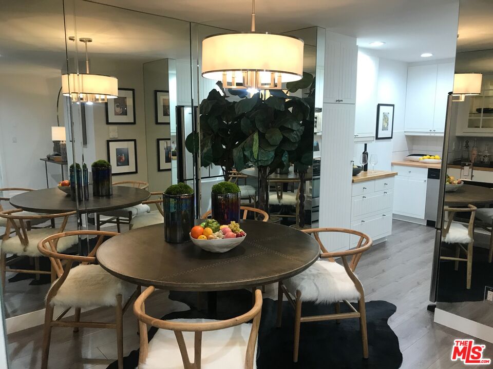 Dining area with a round table, wood chairs, mirrored walls, and an adjacent white kitchen.