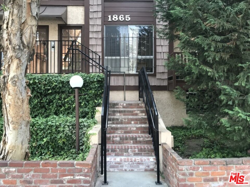 Building entrance at 1865, approached by brick steps with black railings and dense greenery.