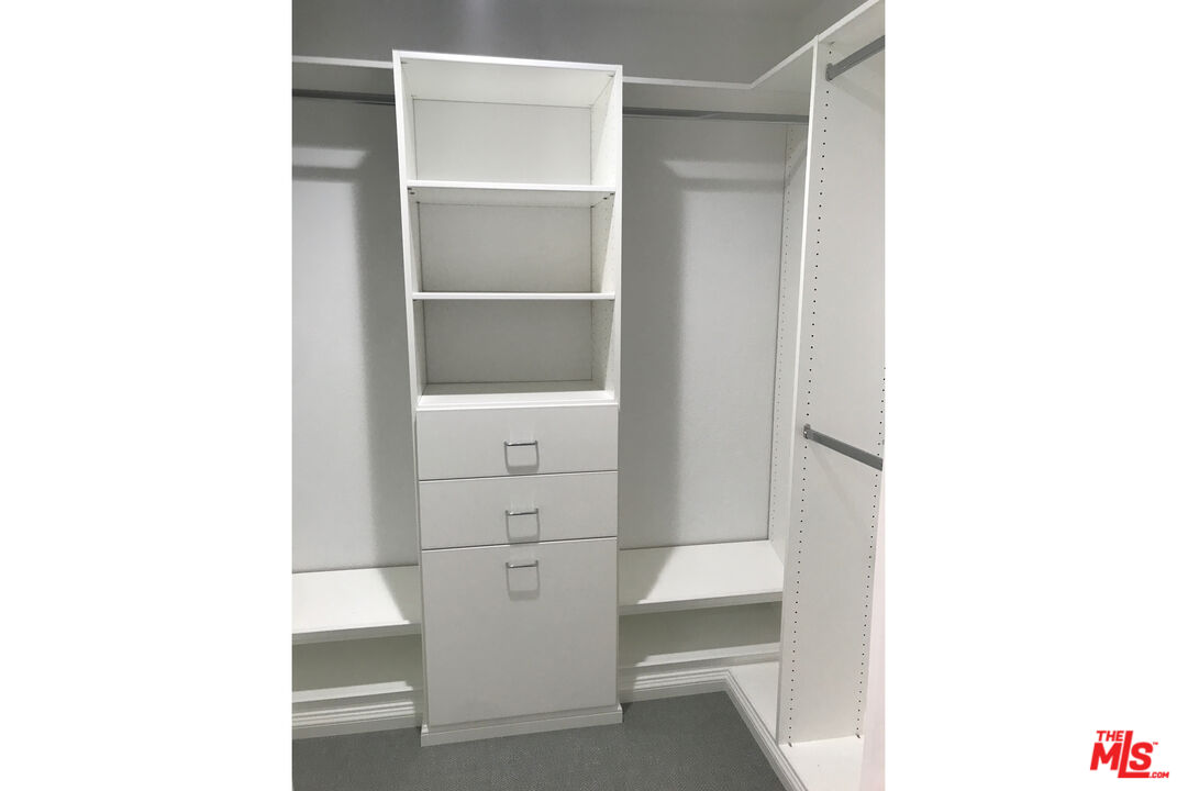 Walk-in closet with built-in white shelving, drawers, and hanging rods.