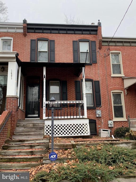 Red-brick rowhouse with black shutters, covered porch, and broad wooden front steps.
