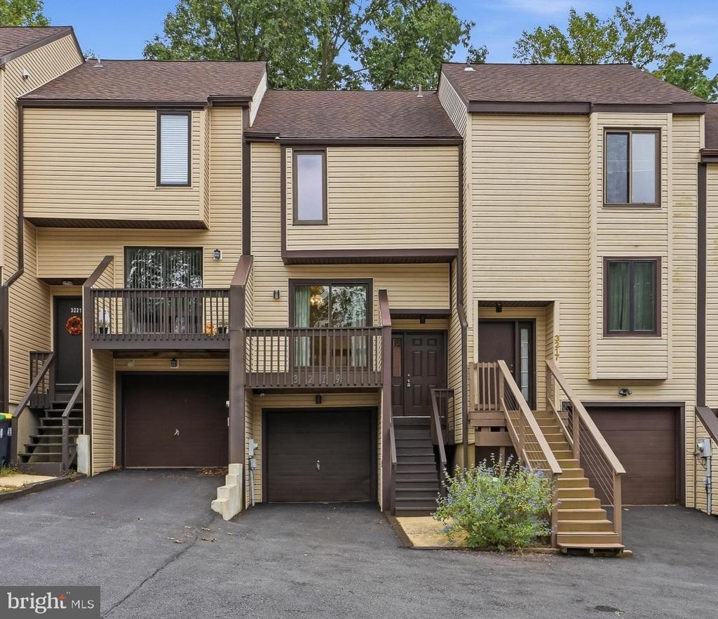 Attached beige townhomes with brown balconies, exterior stairs, and dark garage doors.