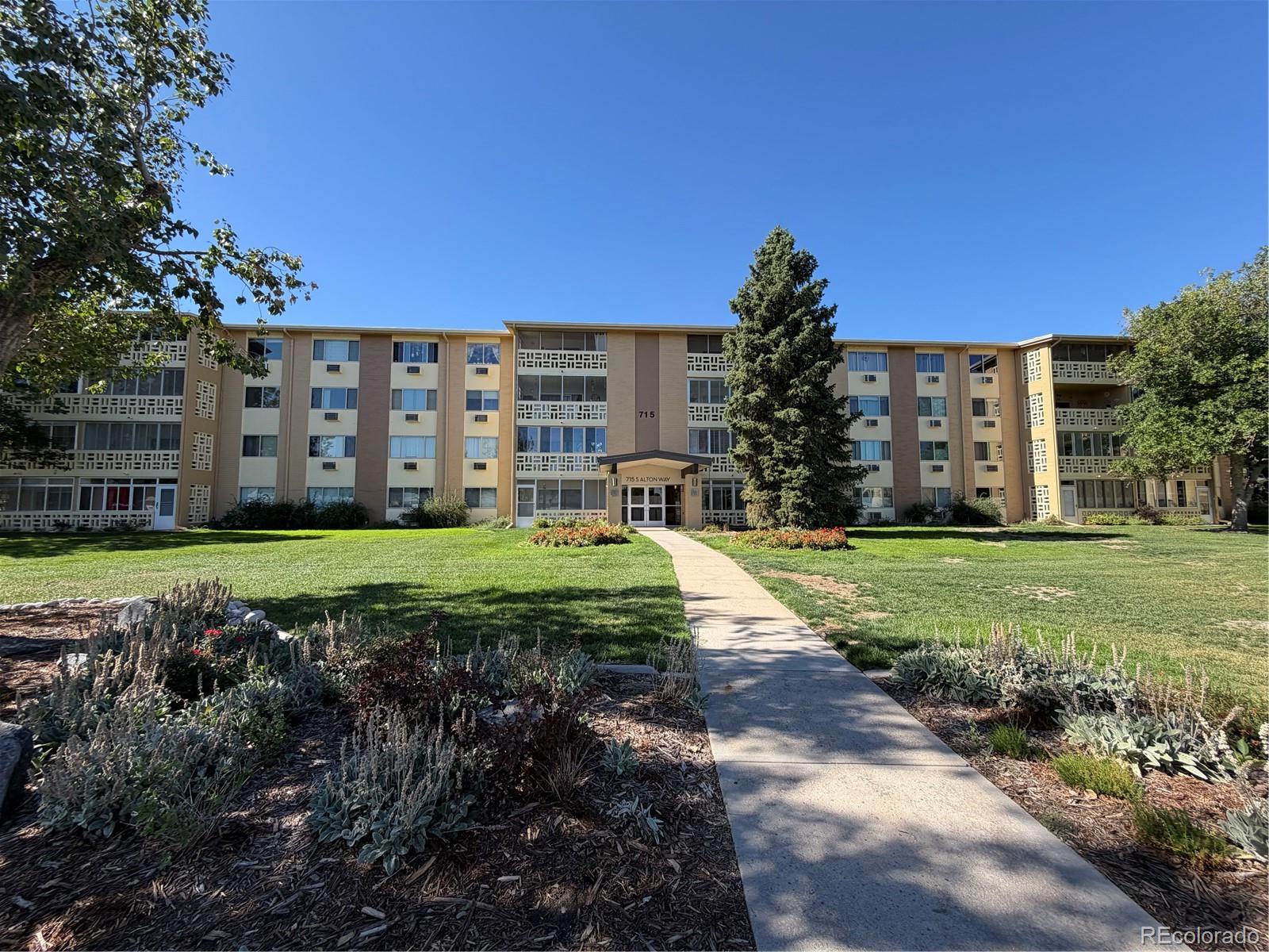 Four-story apartment building at 715 S Alton Way, framed by landscaped gardens and a front walkway.