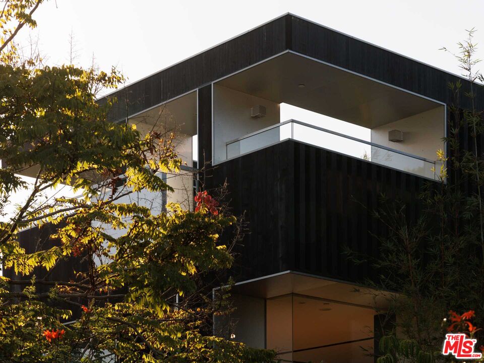 Modern home exterior with dark cladding, an angular roofline, and a glass balcony framed by trees.