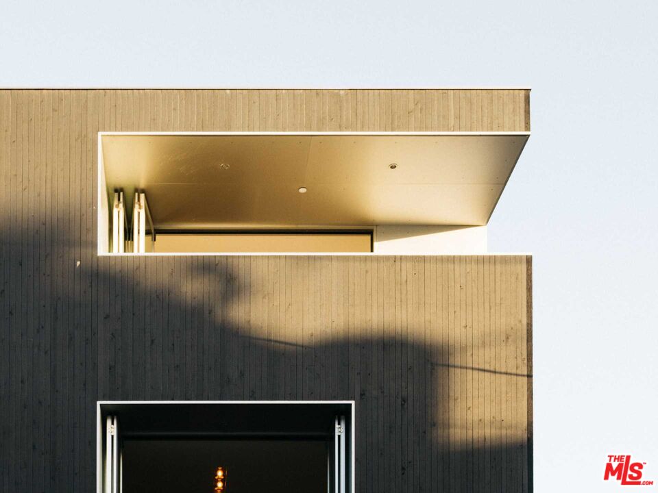Modern home facade with vertical wood cladding and deep rectangular openings in warm sunlight.