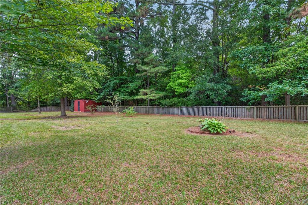 Grassy backyard with a wooden fence, leafy trees, red shed, and hosta bed.