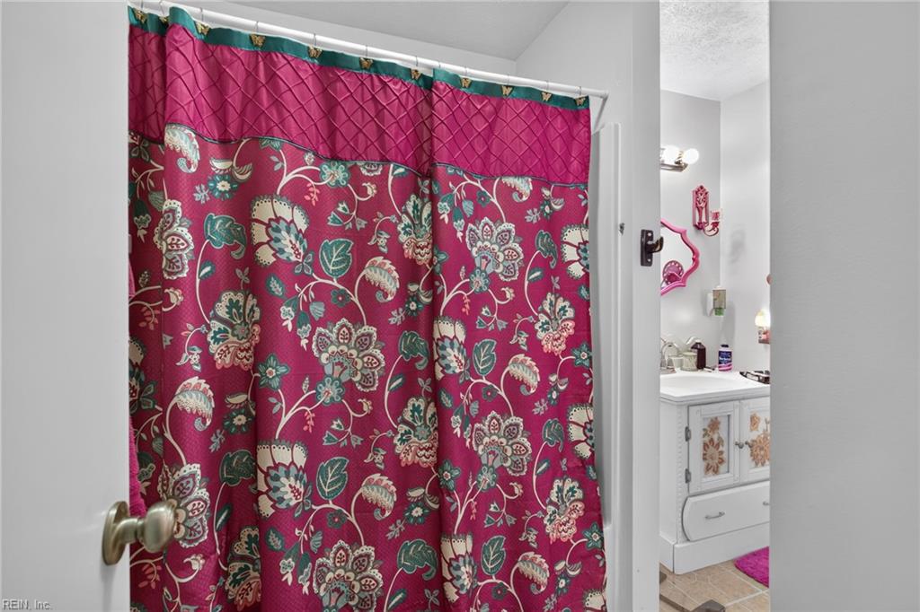 Bathroom with a magenta floral shower curtain and white vanity with floral cabinet panels.