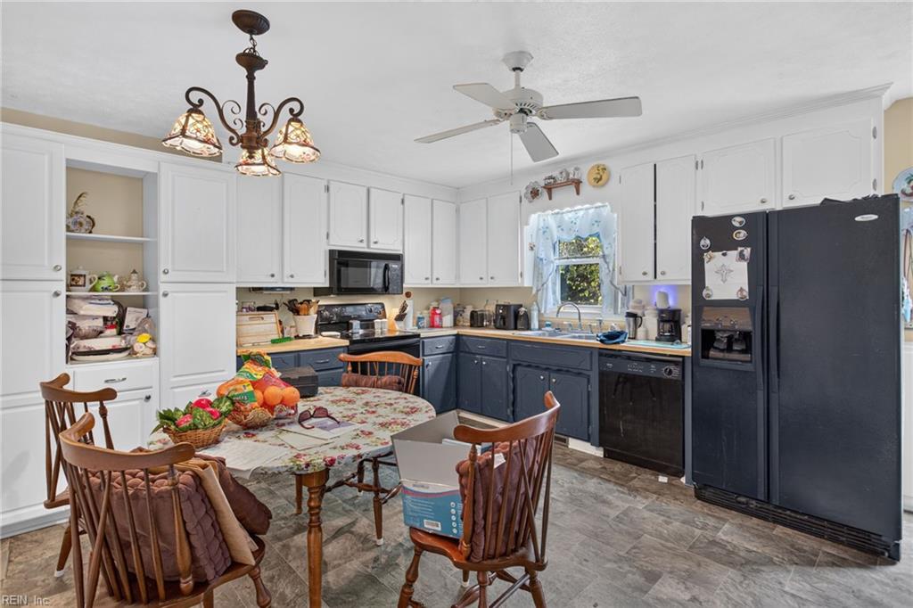 Kitchen with dark blue lower cabinets, black appliances, and a dining table with wooden chairs.