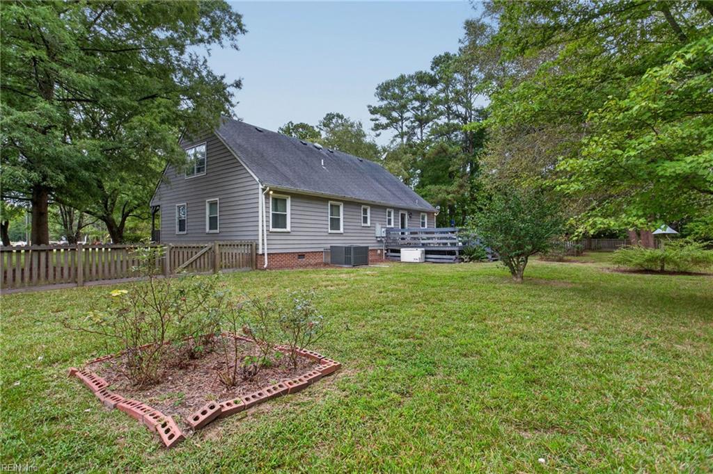 Gray-sided house with a raised deck, grassy yard, mature trees, and fenced garden bed.