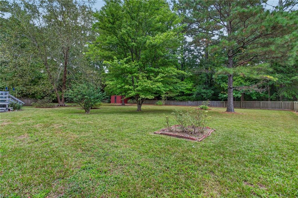 Grassy backyard with mature trees, a wooden fence, red shed, and brick-edged planting bed.