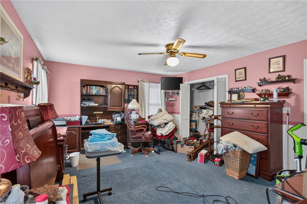 Crowded pink bedroom with blue carpet, wooden dressers, shelving, and an open closet.