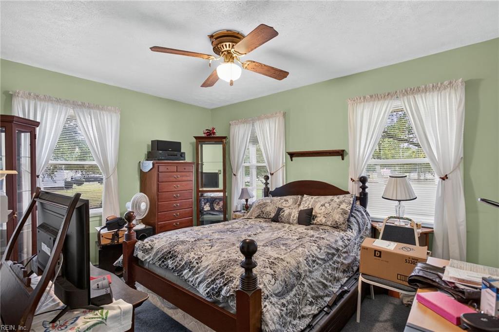 Bedroom with a large wooden bed, pale green walls, and three curtained windows.
