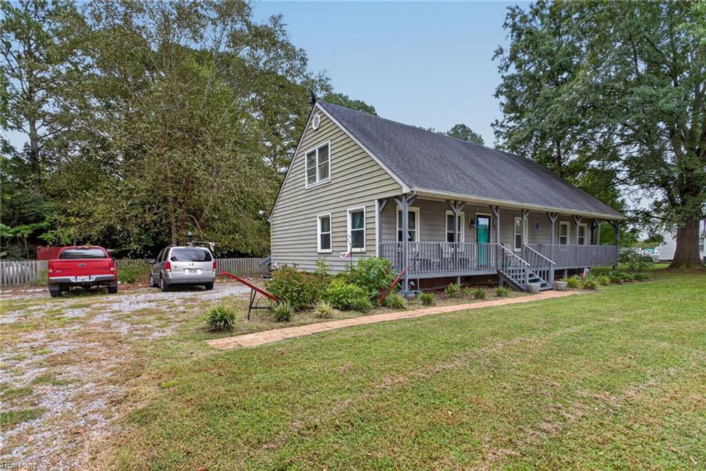 Gray-sided house with a long covered porch, front steps, gravel driveway, and broad lawn.