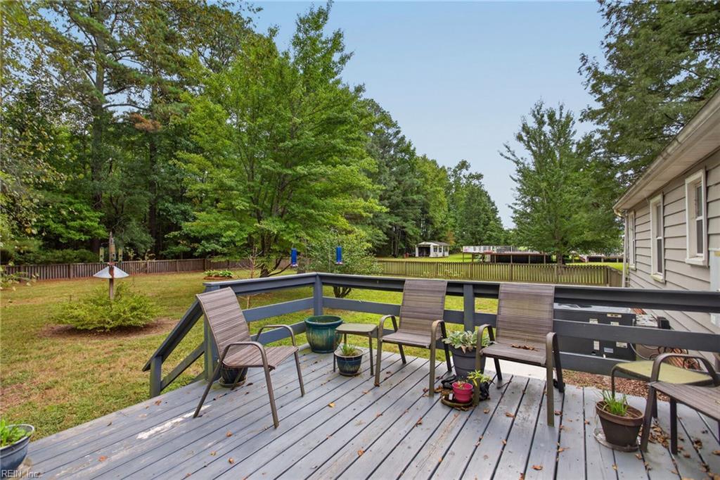 Rear deck with outdoor seating and potted plants overlooking a fenced, tree-lined yard.
