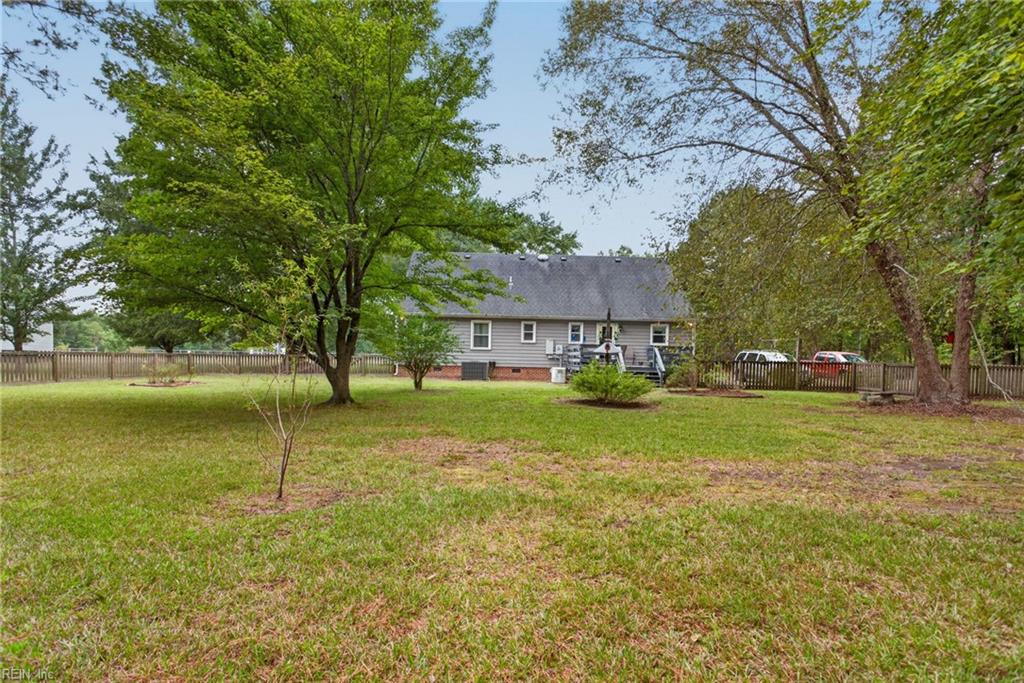 Gray house behind a spacious fenced backyard shaded by mature trees.