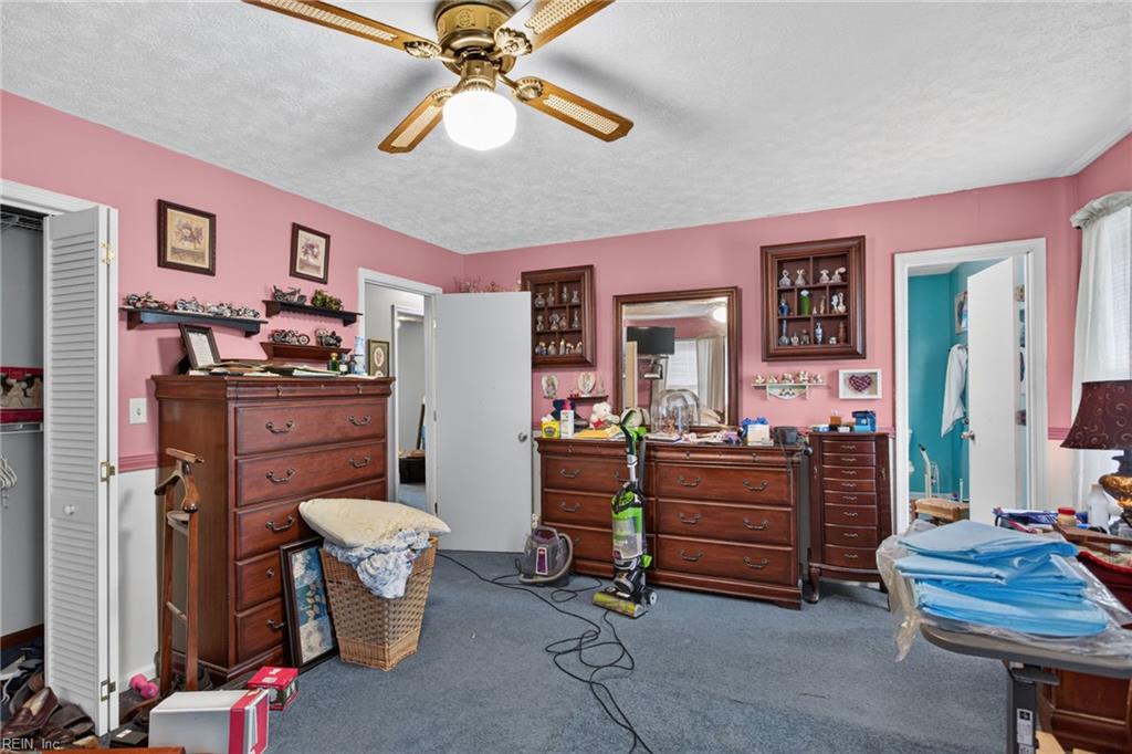 Bedroom with pink walls, blue carpet, wooden dressers, and a ceiling fan.