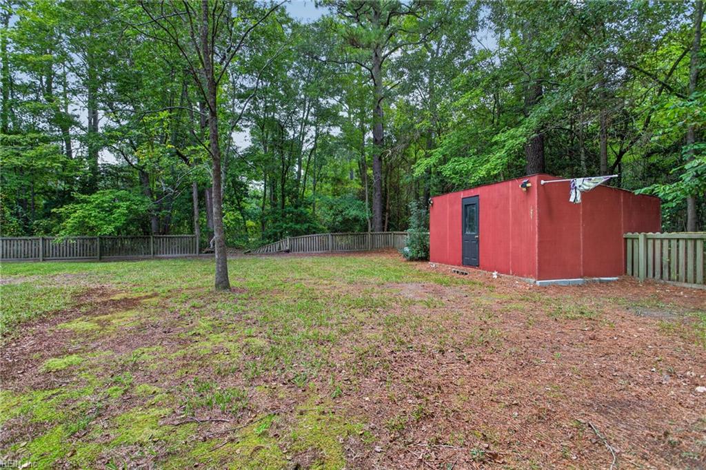 Fenced, wooded backyard with a red outbuilding and patchy grass.
