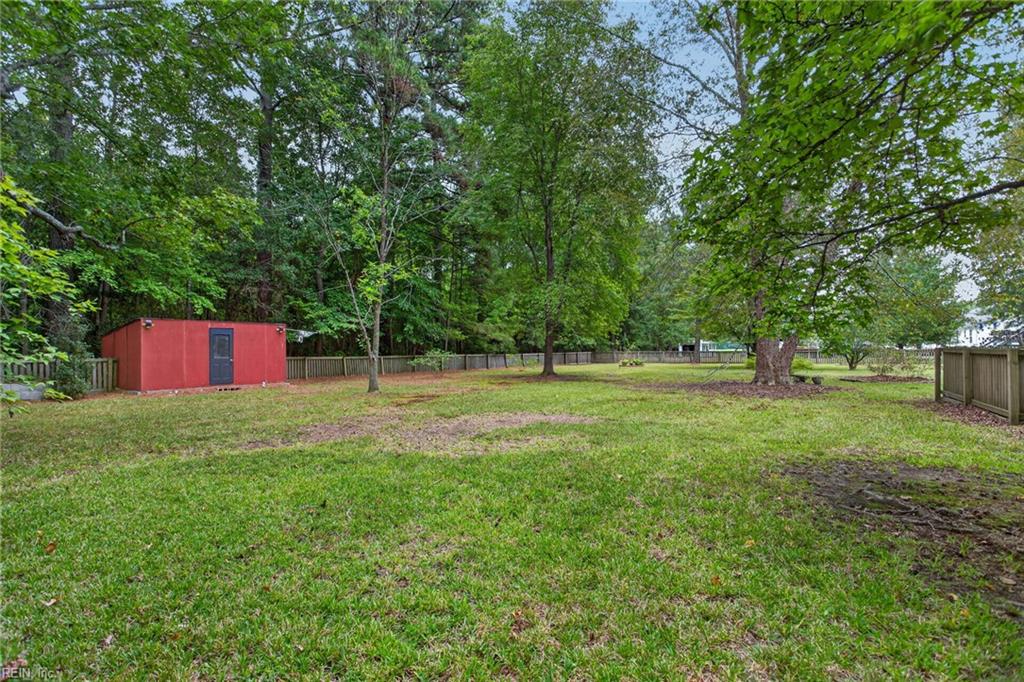 Grassy backyard with mature trees, wooden fencing, and a red shed.