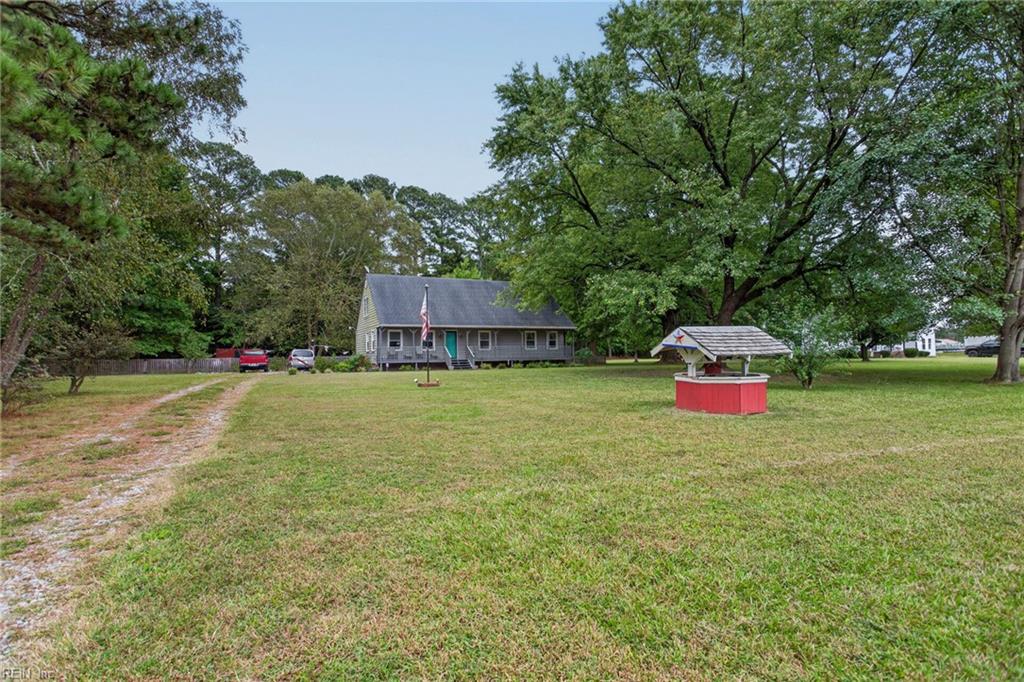 Gray single-story house beyond a broad lawn, with a gravel driveway and a red-and-white garden well.