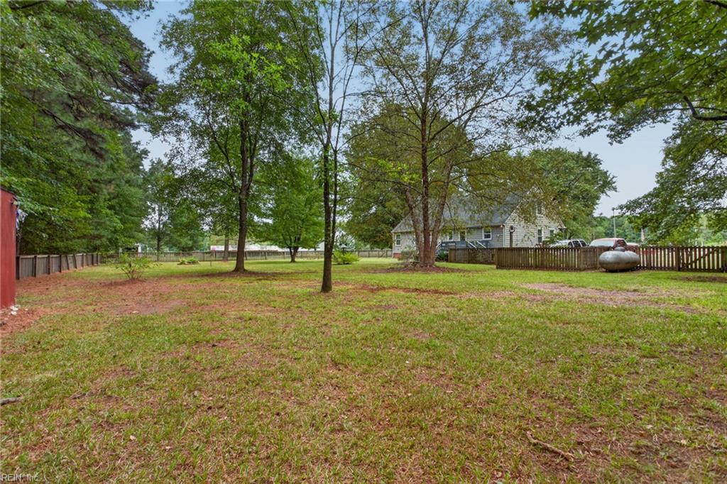 Grassy backyard with mature shade trees, wooden fencing, and the house in the background.