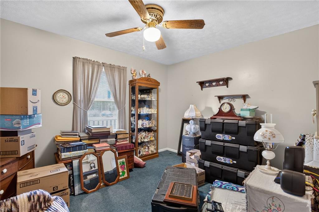Cluttered room with stacked boxes, framed pictures, display shelves, and a ceiling fan.